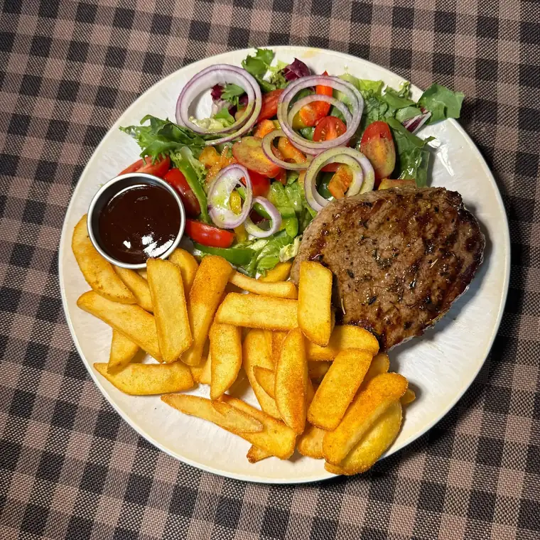 Talerz z grillowanym mięsem, domowymi frytkami i sałatką na obrusie w kratę